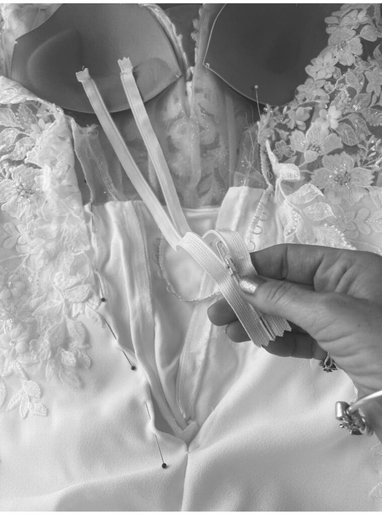 Bridal seamstress replacing a zip and button loops inside a wedding dress after structural fit adjustments.