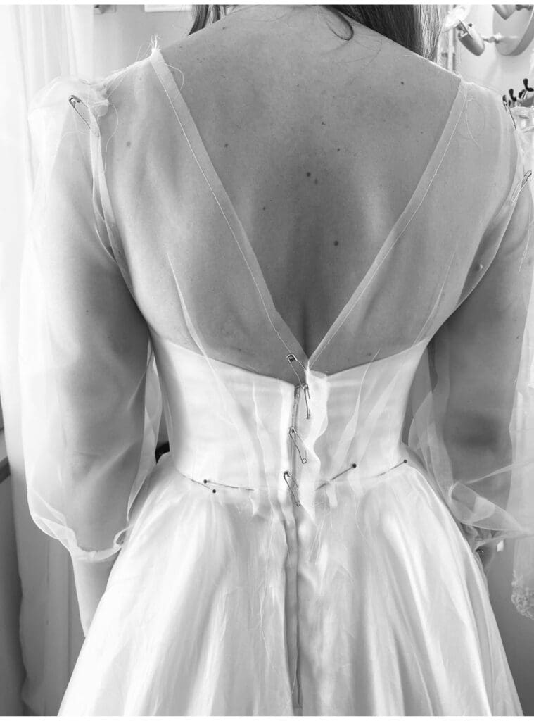 Organza overlay being pinned into place during a wedding dress redesign, creating a new bodice and skirt over the original gown.