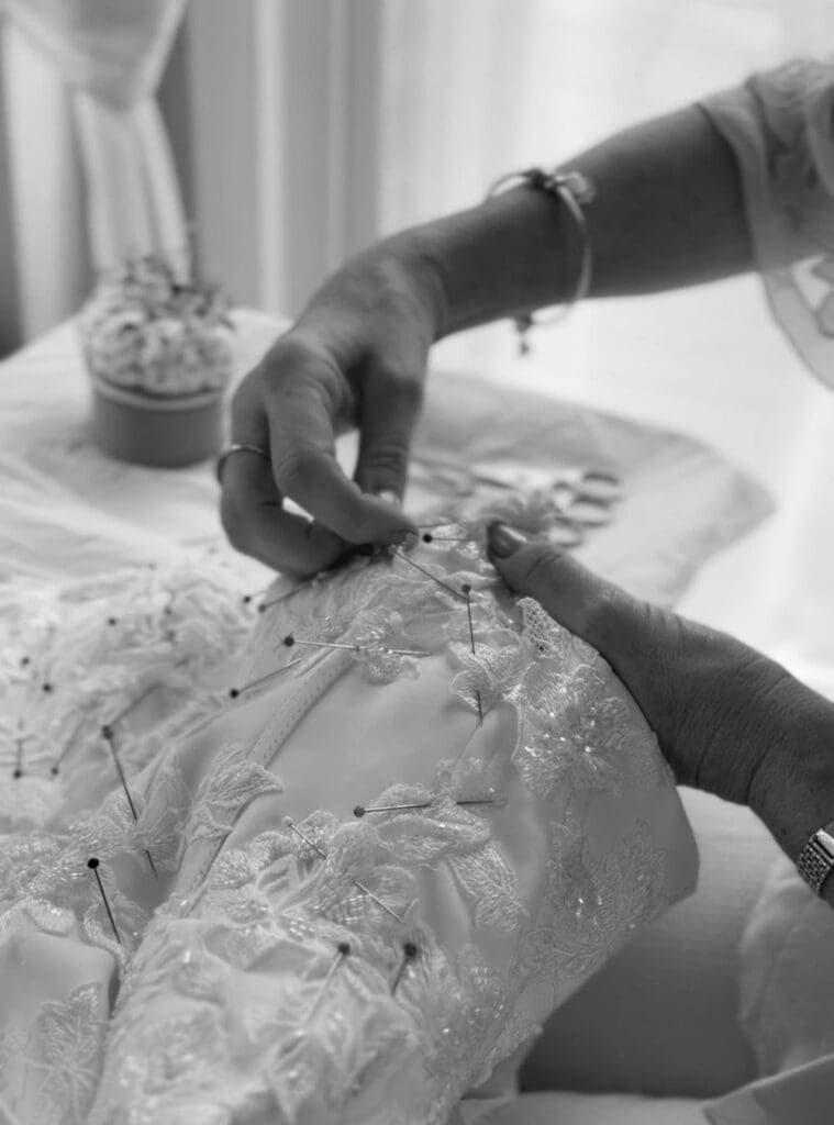 Lace appliqué being carefully repositioned, pinned and hand sewn onto a wedding dress after seam alterations.