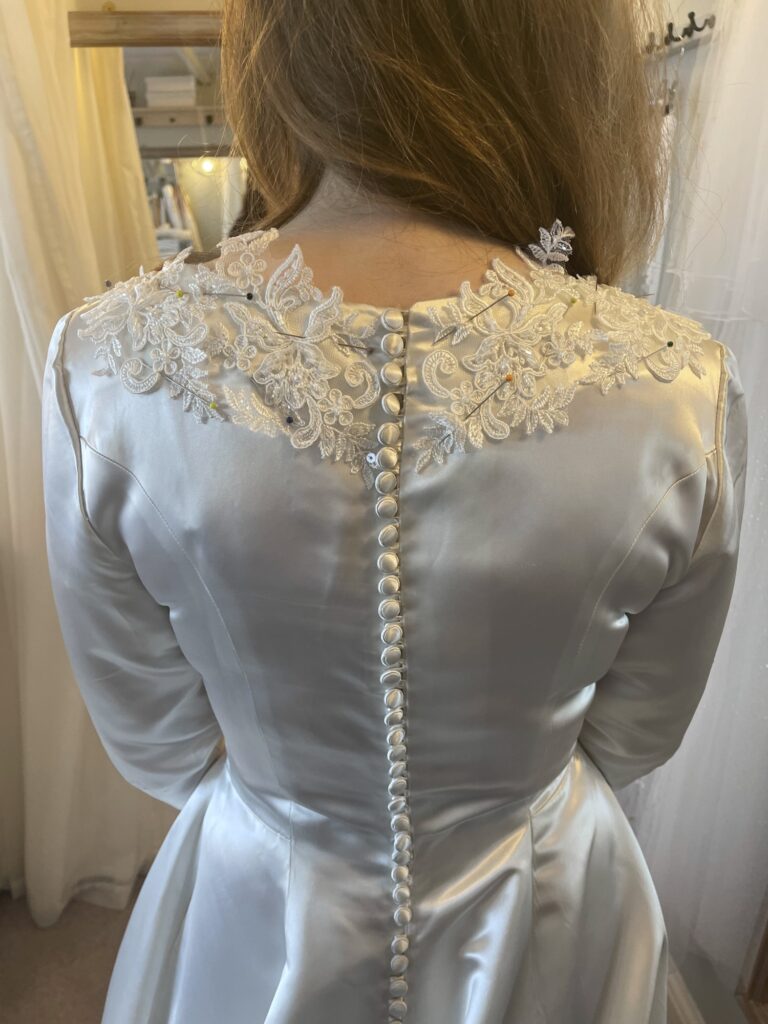 Lace being positioned on the back of Fiona’s heirloom wedding dress during a fitting